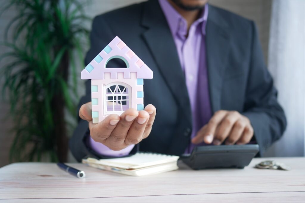 man in purple suit jacket using laptop computer holding a small miniature house