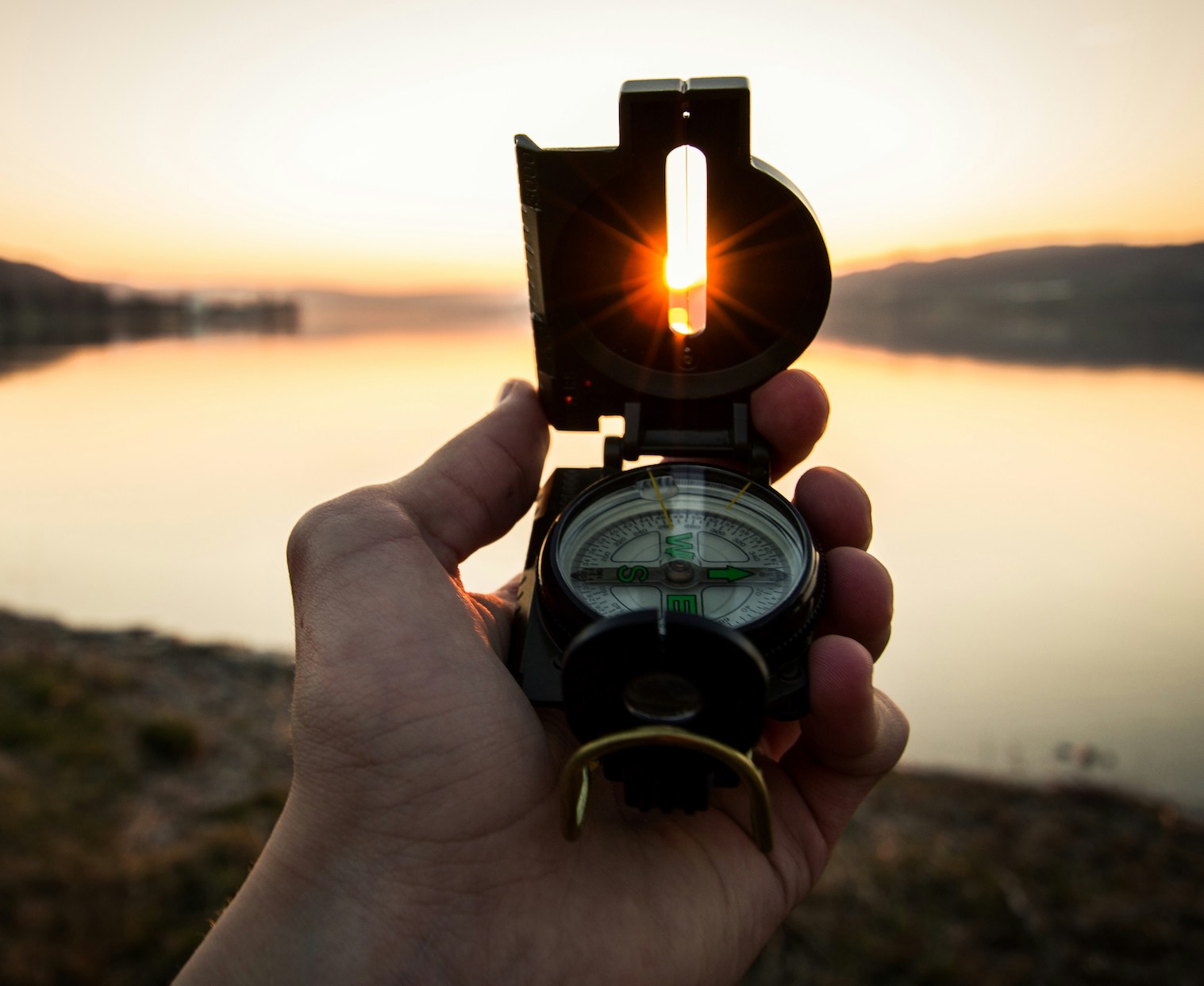 man holding compass with lake and hills in background